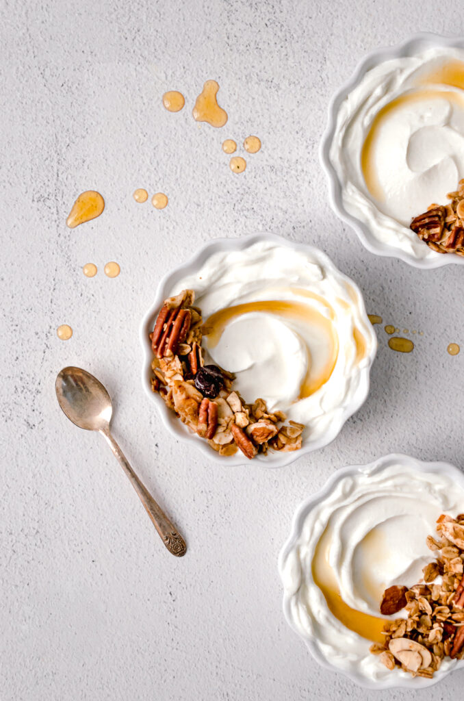 three bowls of yogurt with homemade maple nut granola and splashes of maple syrup everywhere