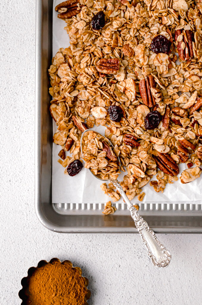 homemade maple nut granola on parchment lined baking sheet with silver spoon