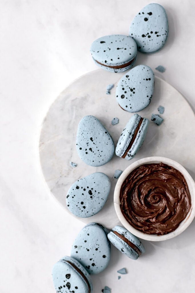 Robin's Egg Macarons with a bowl of chocolate french buttercream on marble 