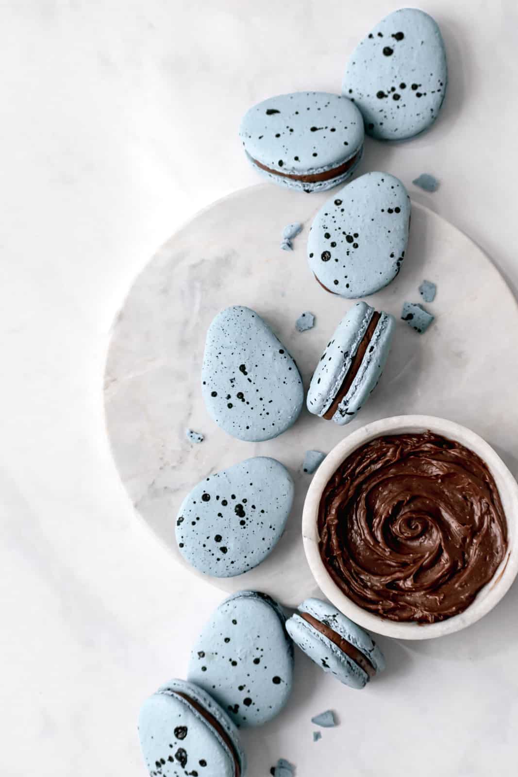 Robin's Egg Macarons with a bowl of chocolate french buttercream on marble.