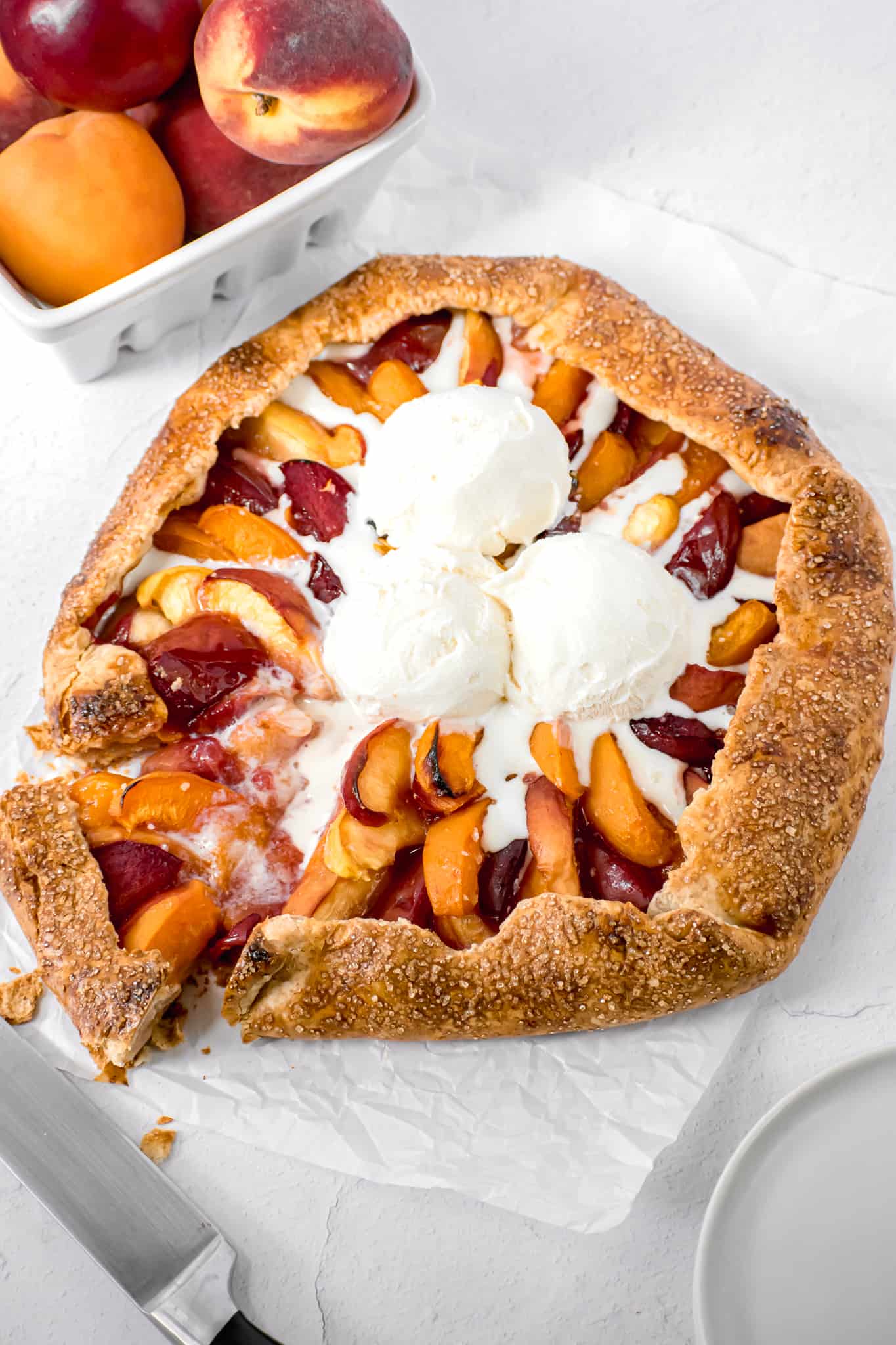 stone fruit galette on parchment paper with ice cream on top.