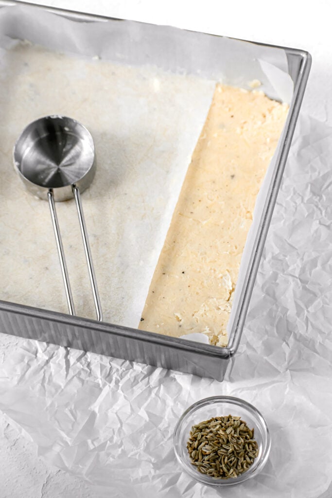 parmesan shortbread in square pan being smoothed.