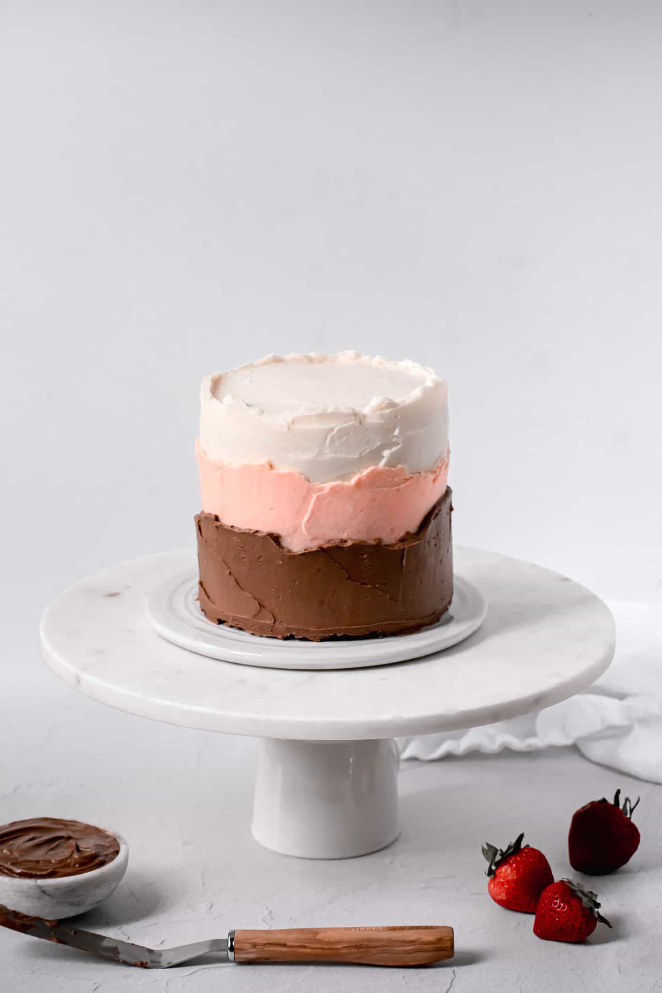 neapolitan cake with swiss meringue buttercream on white cake stand.
