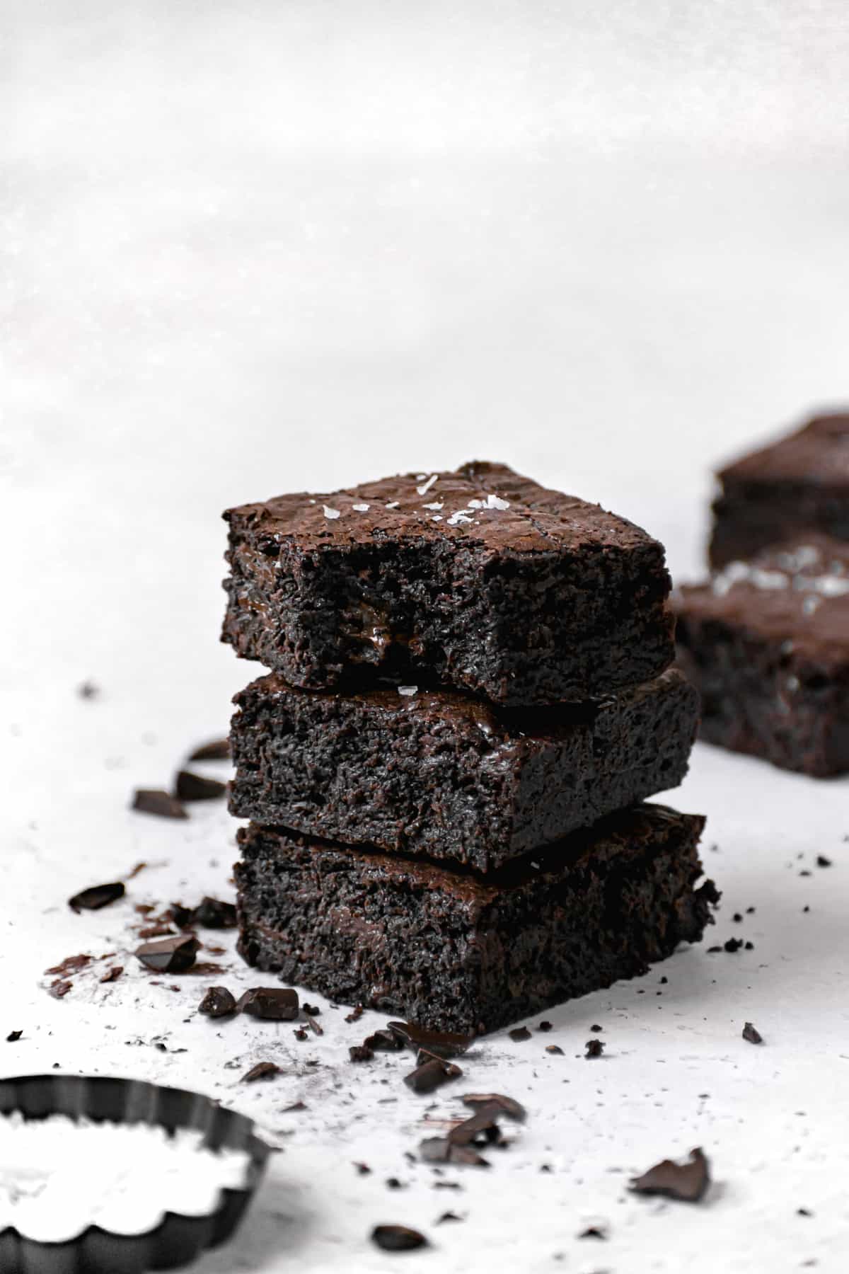 three brown butter brownies stacked with chopped chocolate.