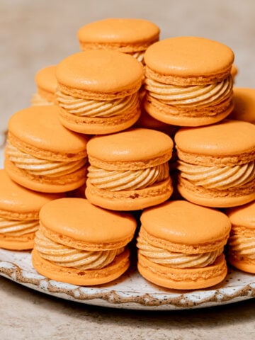 pumpkin macarons stacked on plate.