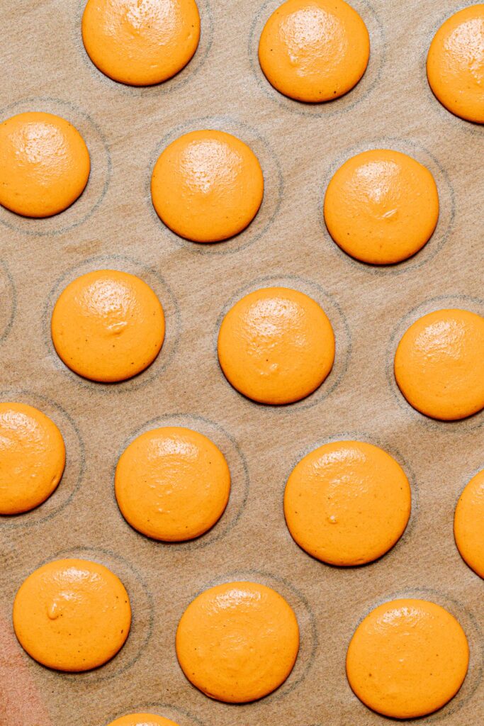 Pumpkin Macaron batter piped onto baking sheet.