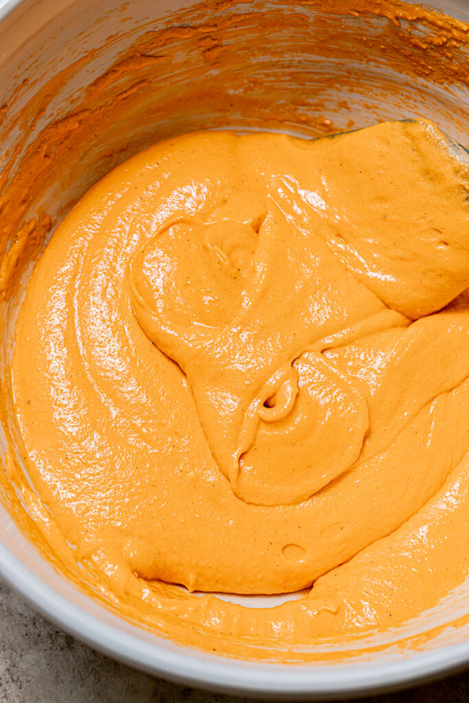 orange colored macaron batter in bowl.