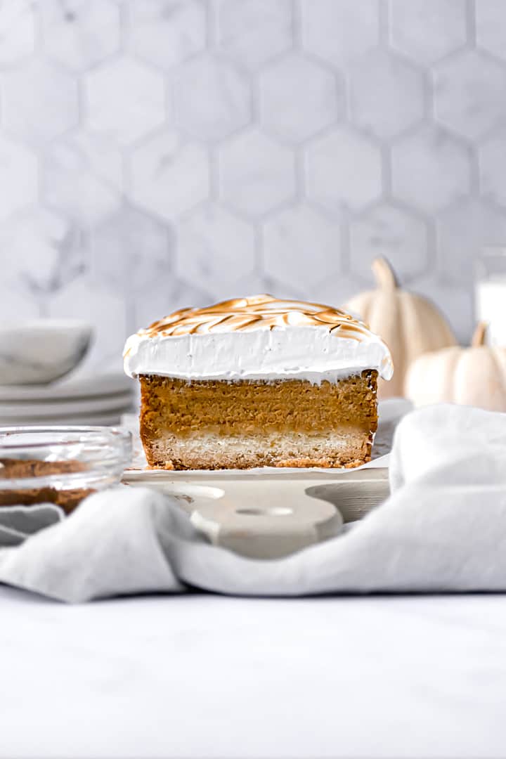 pumpkin pie bars on rectangular cutting board with mini pumpkins in the background.