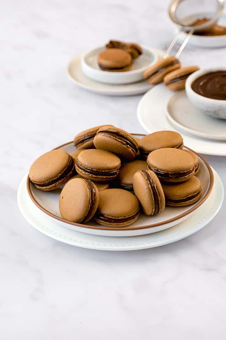 espresso macarons filled with chocolate caramel ganache on two stacked plates.