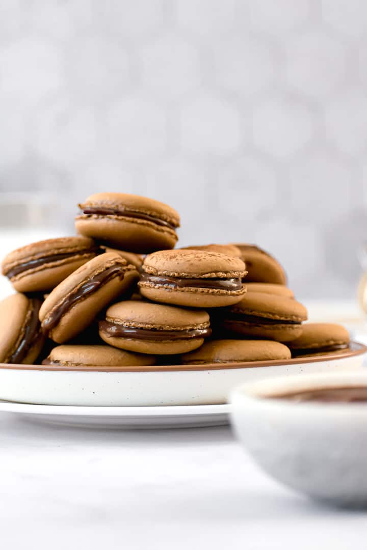 espresso macarons on a plate with a bowl of ganache upfront.