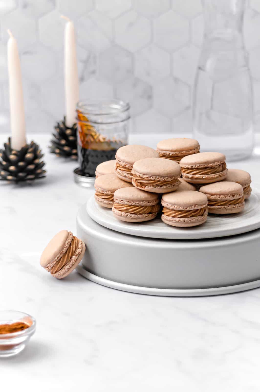 macarons stacked on top of overturned cake pan with candles and a jar of molasses in the background.
