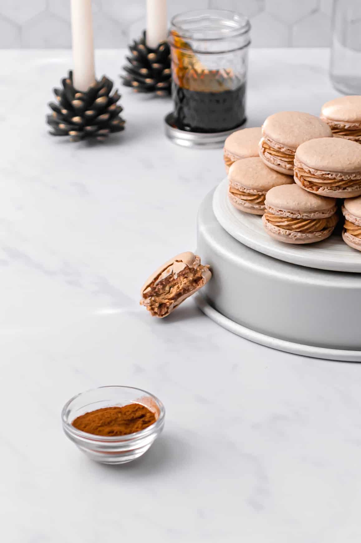 macarons stacked on top of overturned cake pan with candles and a jar of molasses in the background.