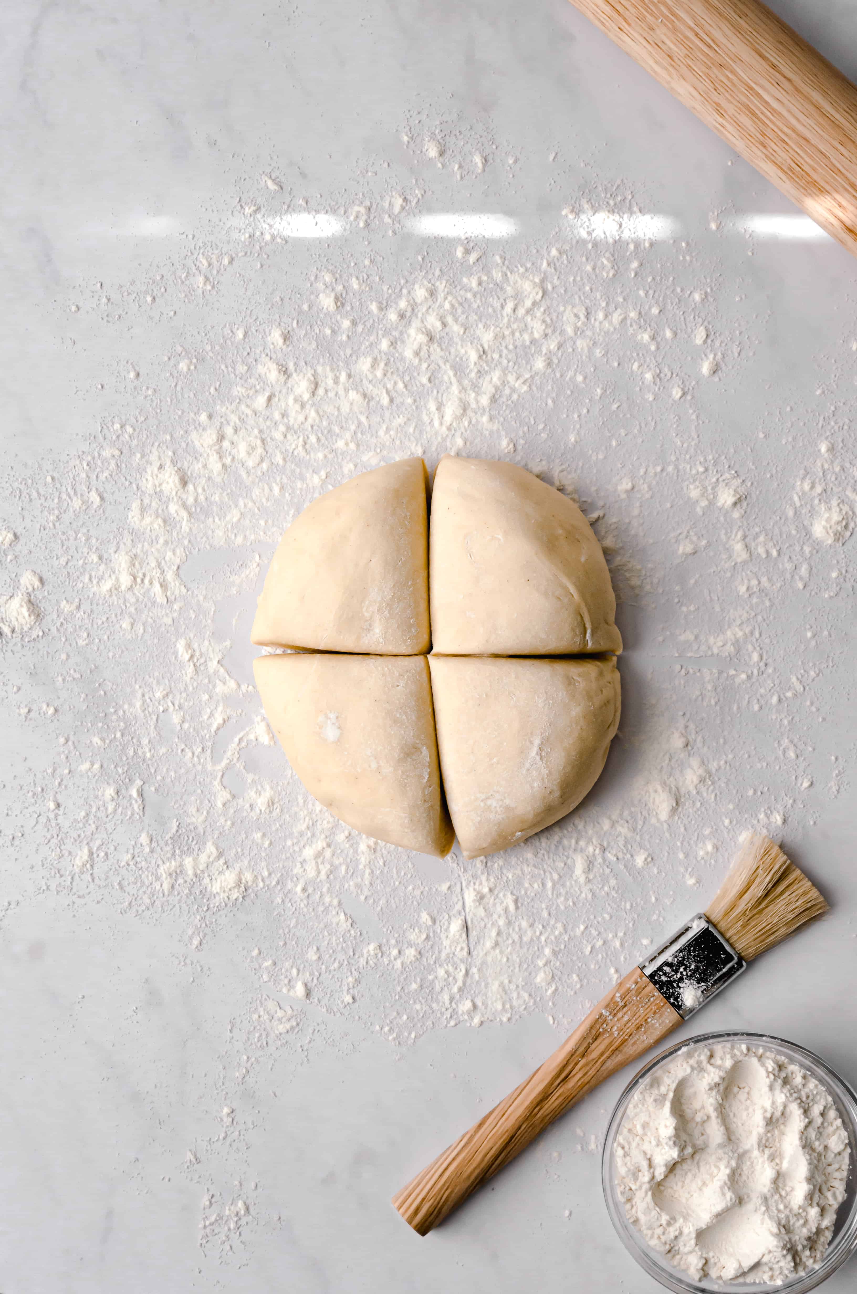 brioche dough cut into quarters on flour dusted marble surface.