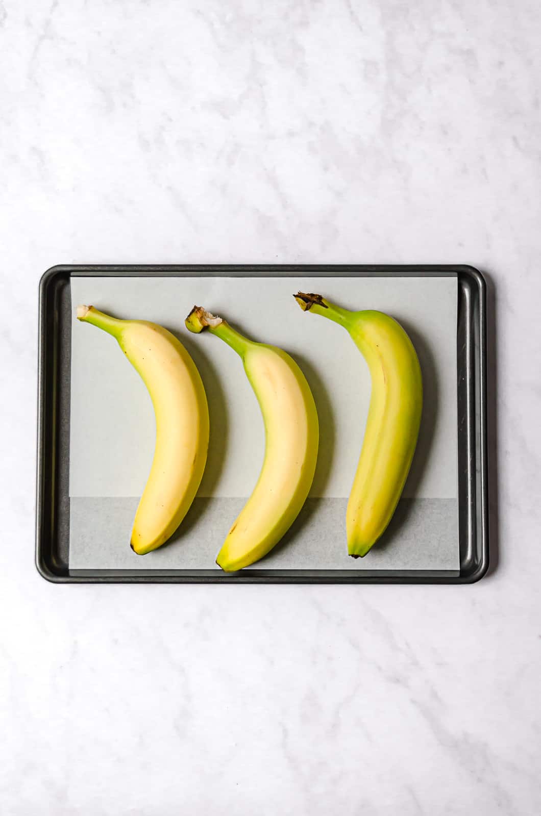 three yellow bananas on parchment lined baking sheet.