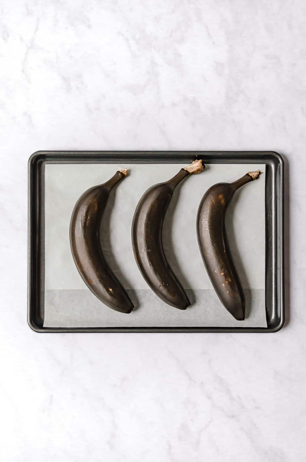 three roasted bananas on parchment lined baking sheet.