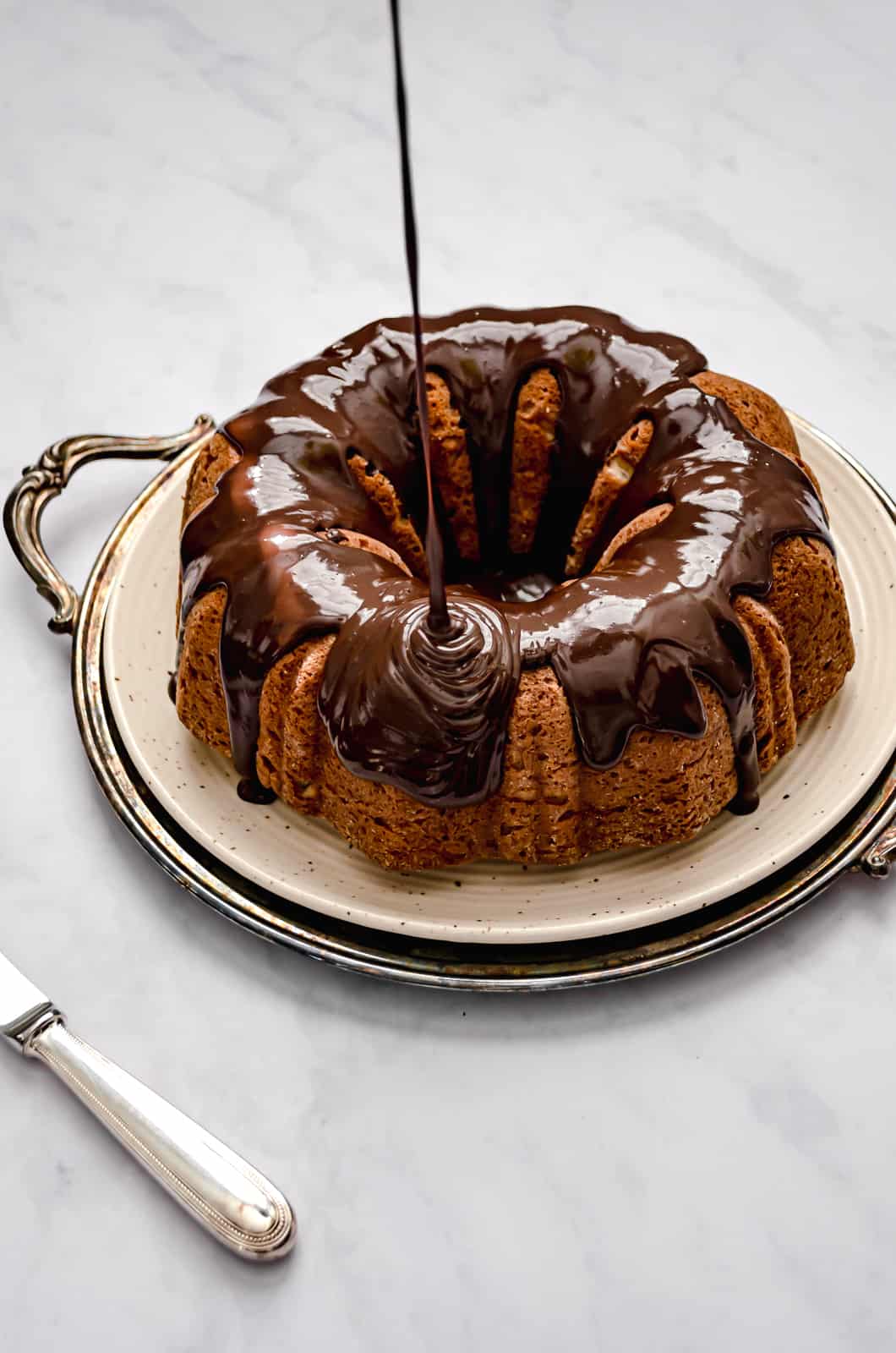 roasted banana bundt cake with chocolate glaze being drizzled on top.