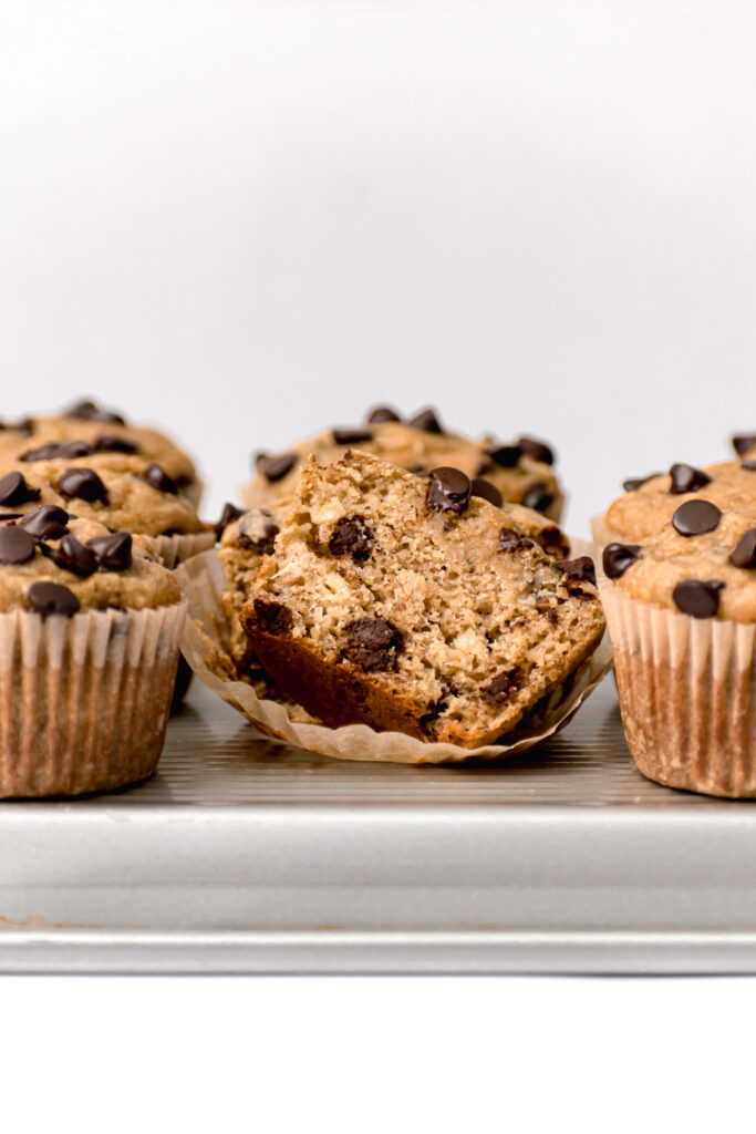 banana tahini chocolate chip muffins on silver baking sheet with one muffin cut in half