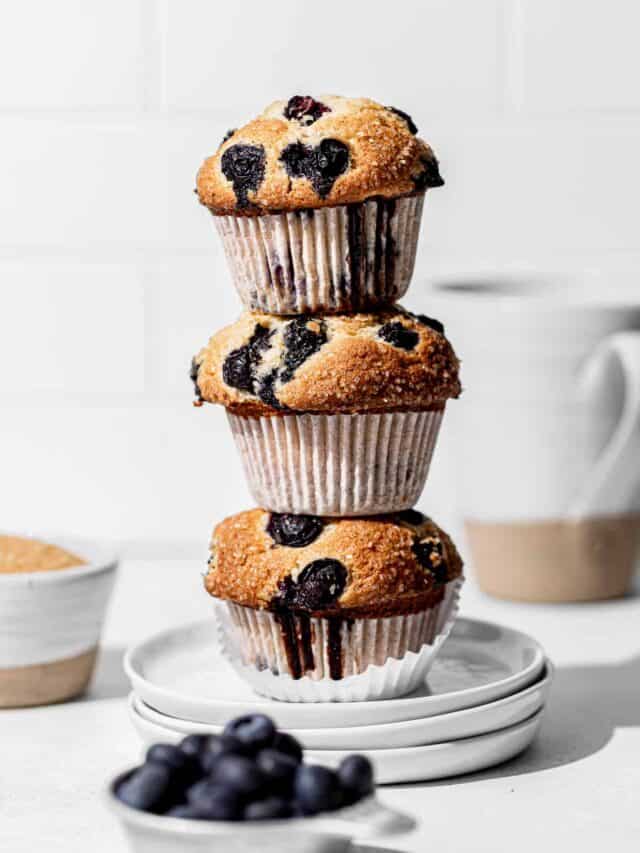 three blueberry muffins stacked on white plates.