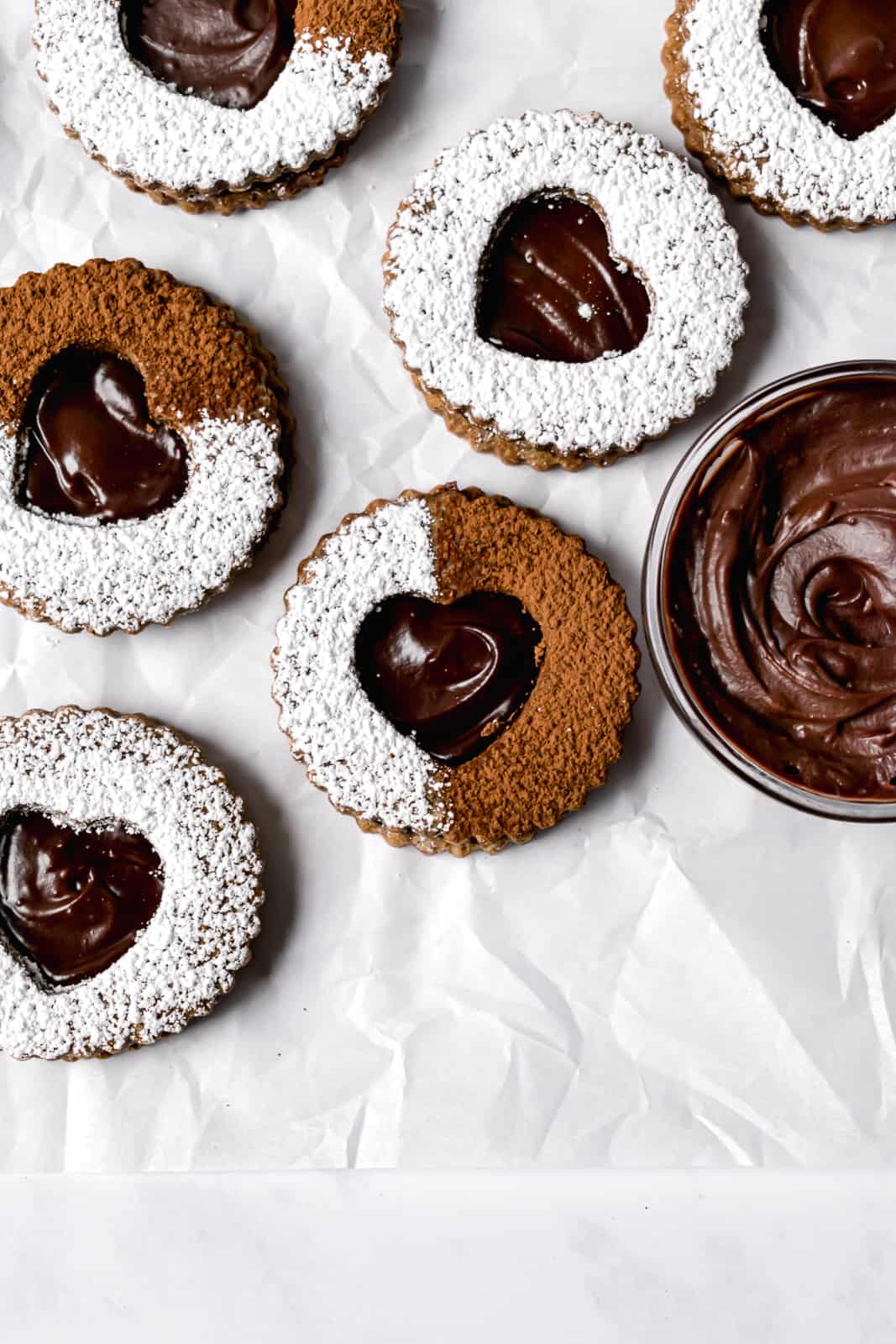 chocolate espresso linzer cookies with powdered sugar and cocoa powder on parchment paper.