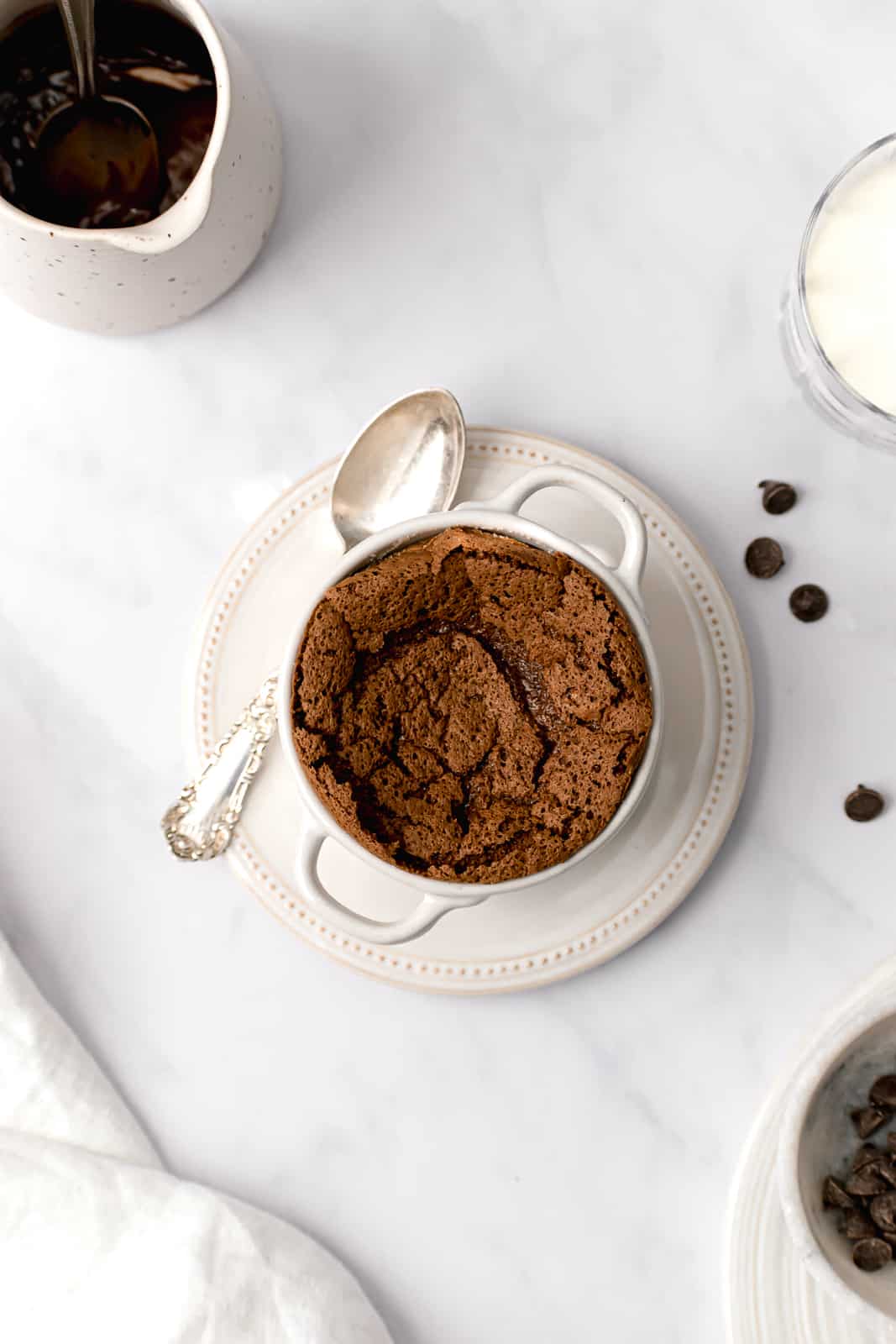 mini chocolate soufflé for one in white ramekin on top of white plate with silver spoon.