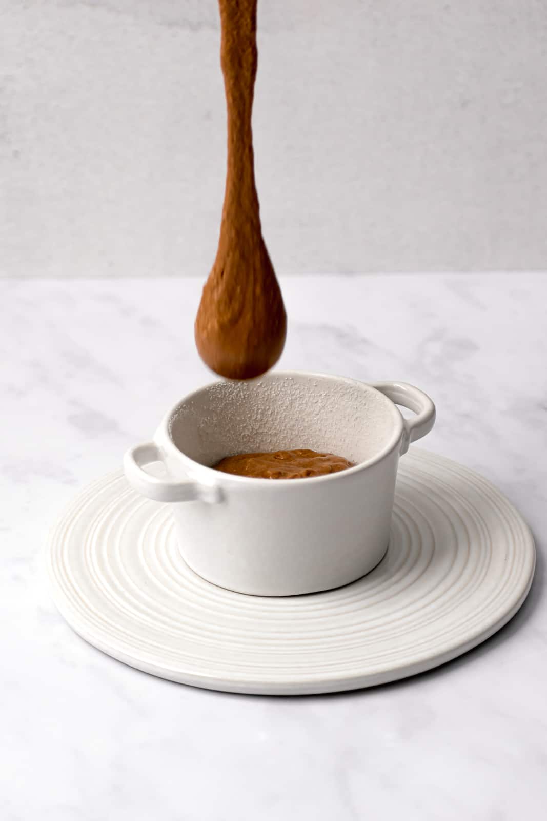 soufflé batter being poured into a white ramekin on top of a white trivet