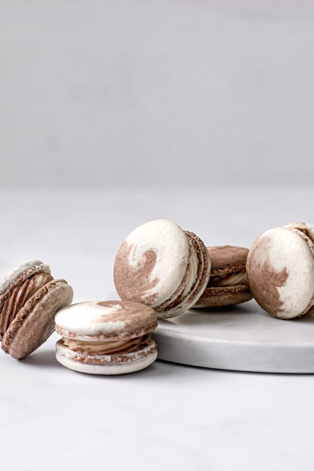 Chocolate & Vanilla Swirled Macarons leaned up against each other on marble.