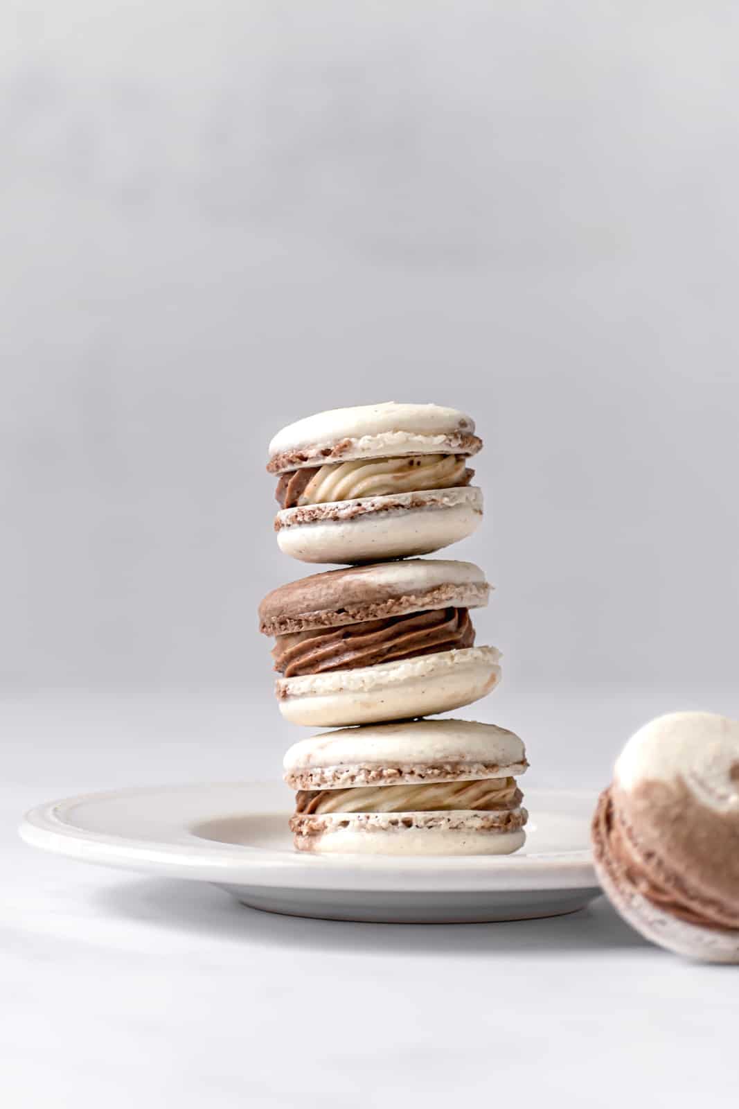 three Chocolate & Vanilla Swirled Macarons stacked on a white plate.