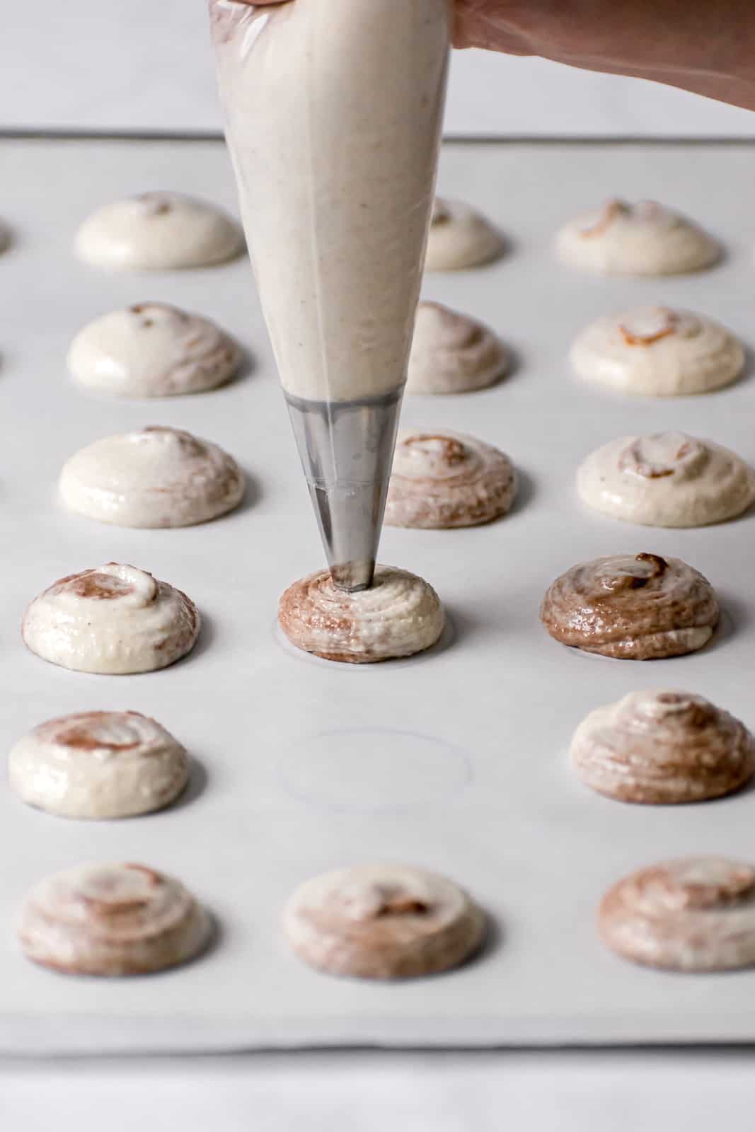 macaron batter being piped on parchment lined baking sheet.
