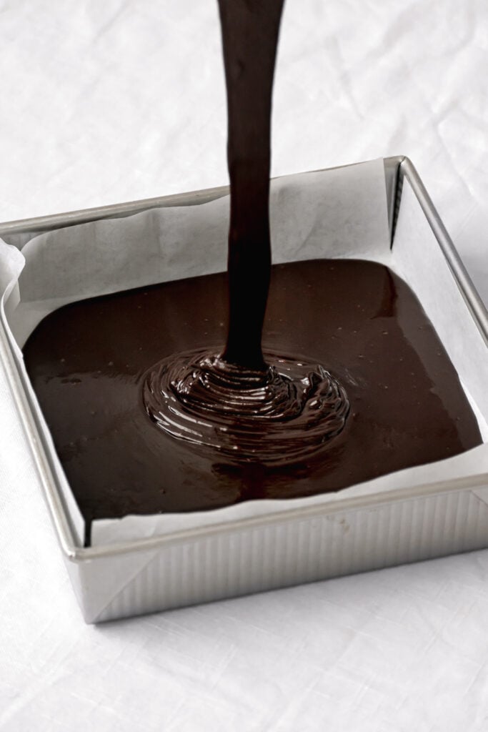 chocolate cake batter being pour into square pan