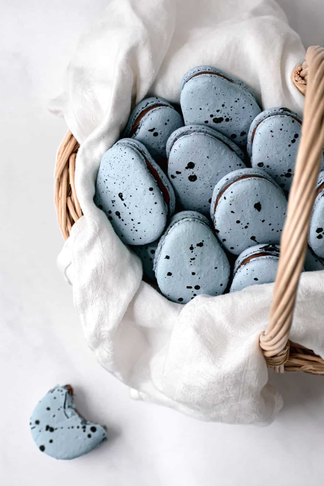 Robin's Egg Macarons with chocolate french buttercream in a basket lined with a white linen.