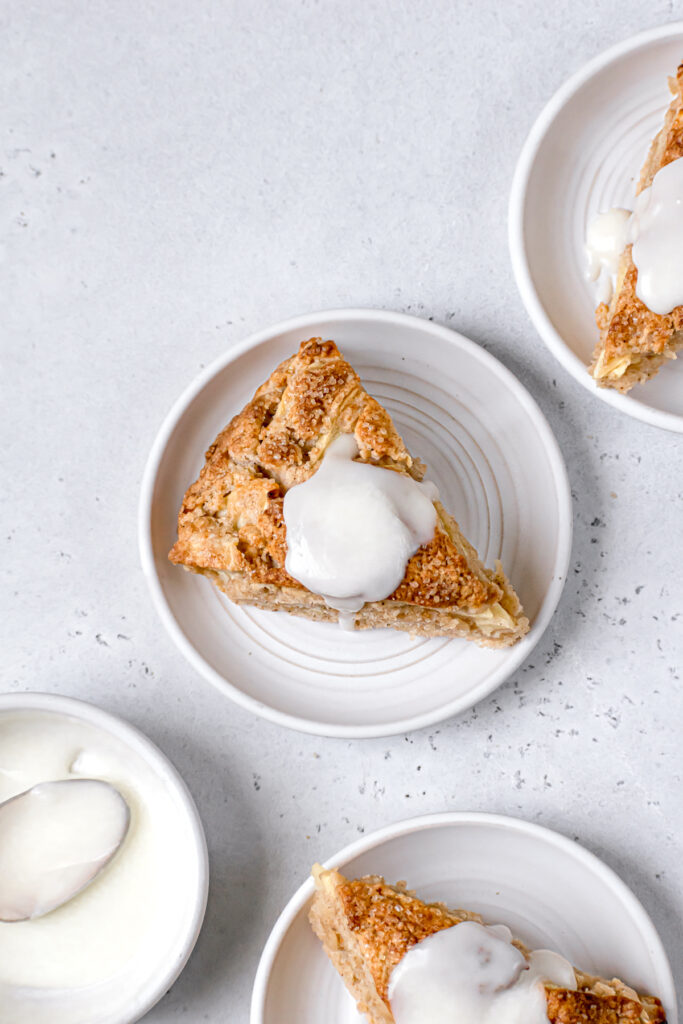 three apple cinnamon scones on white plates with a bowl of glaze