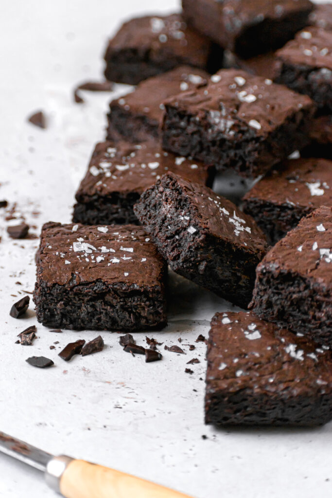 pile of chewy brownies on white parchment paper with flaky sea salt