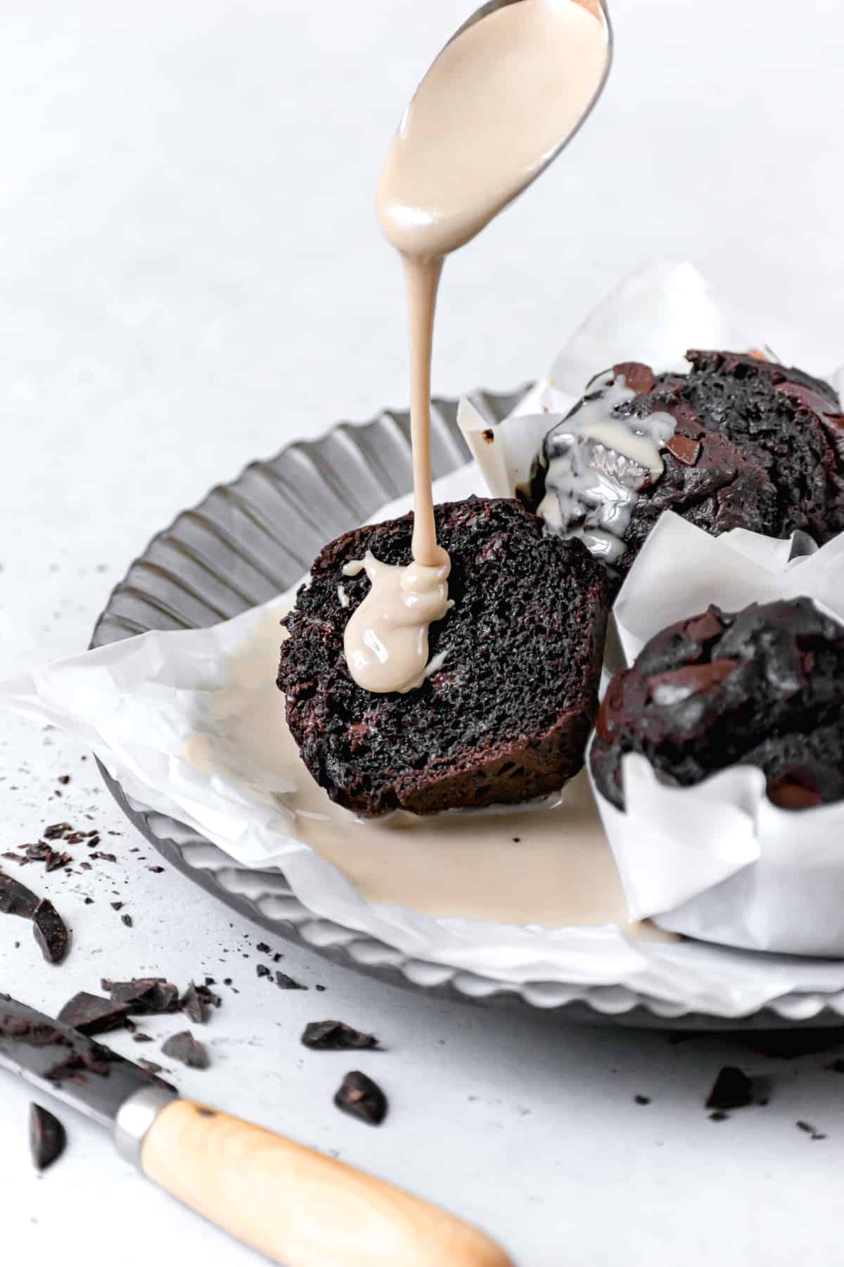one double chocolate tahini muffin cut open on a plate with tahini being drizzled on top.