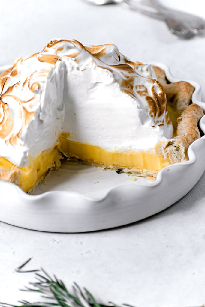 cut lemon meringue pie with fresh rosemary crust in white pie dish
