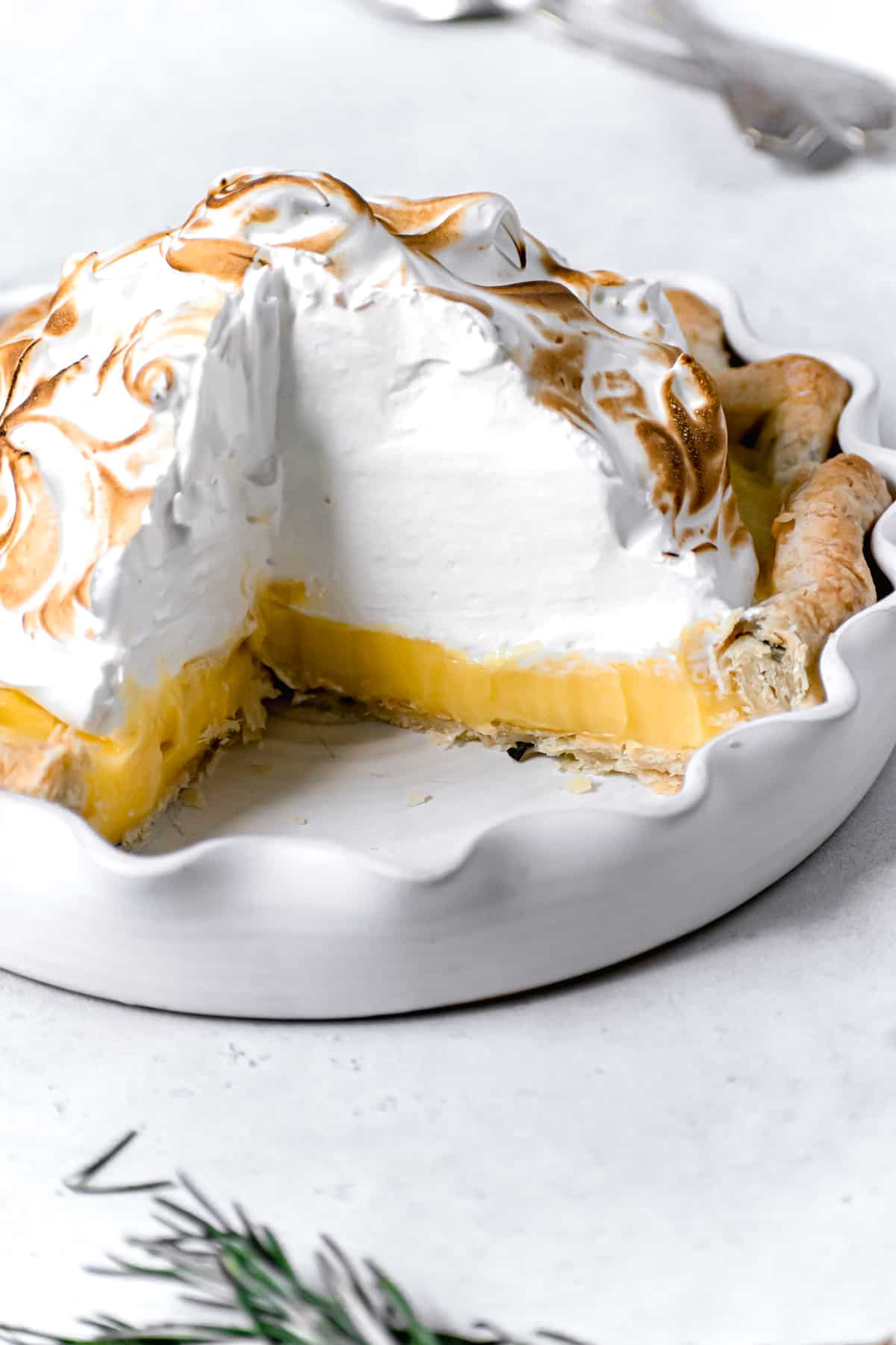 cut lemon meringue pie with fresh rosemary crust in white pie dish.