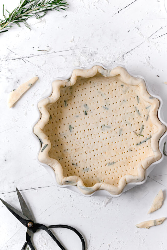 pie dough in white dish, with crimped edges and docked all over 
