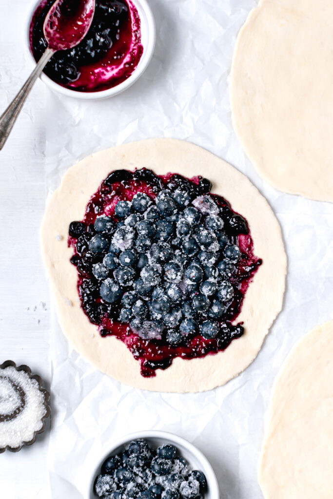 partly assembled mini blueberry galettes on white parchment paper