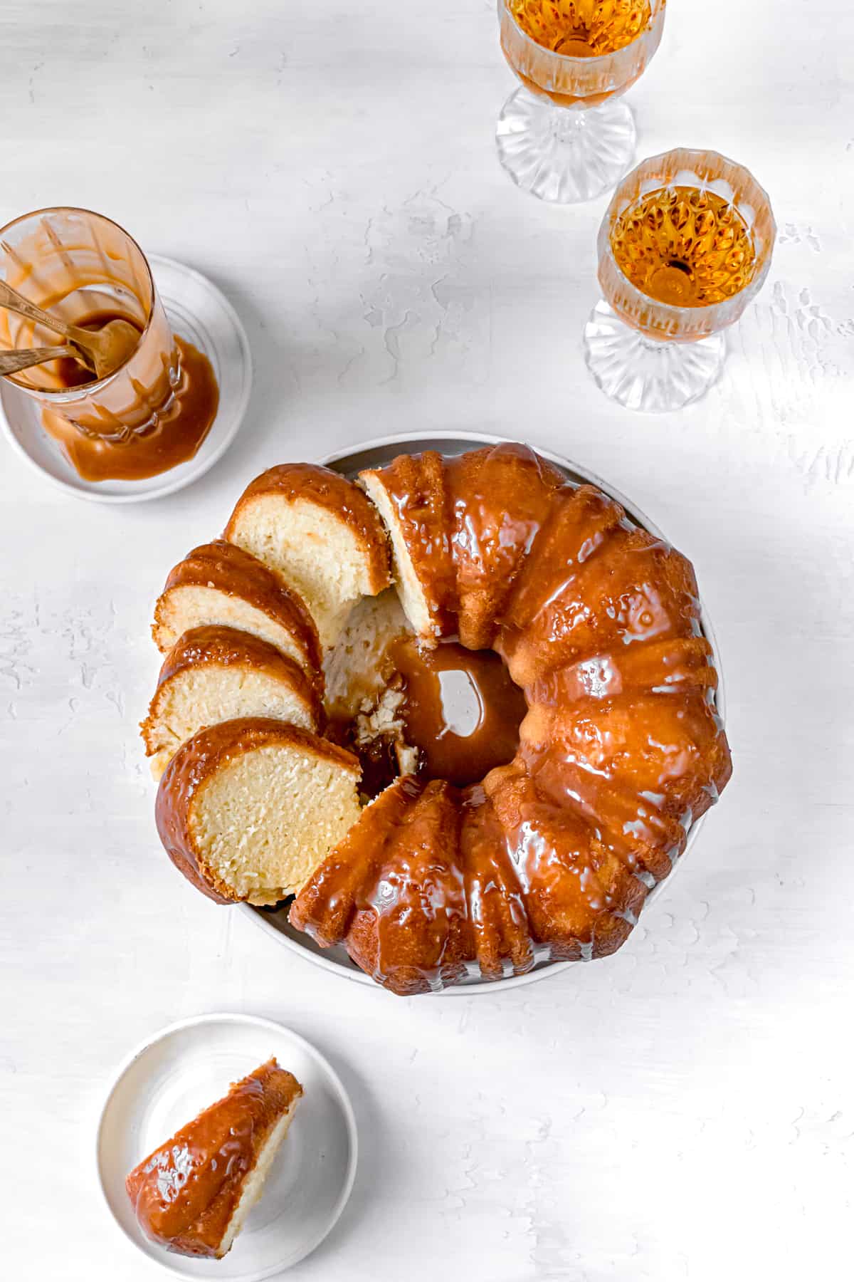 sliced bundt cake with glasses of rum and cup of caramel sauce.
