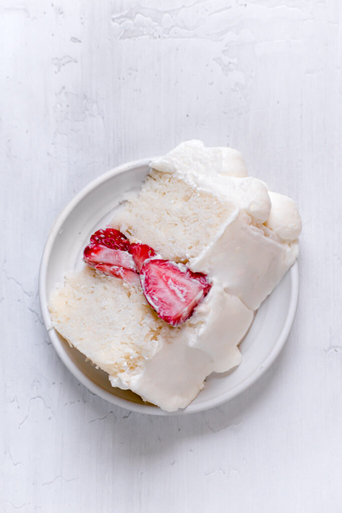 one slice of white cake with strawberries and mascarpone frosting on white plate