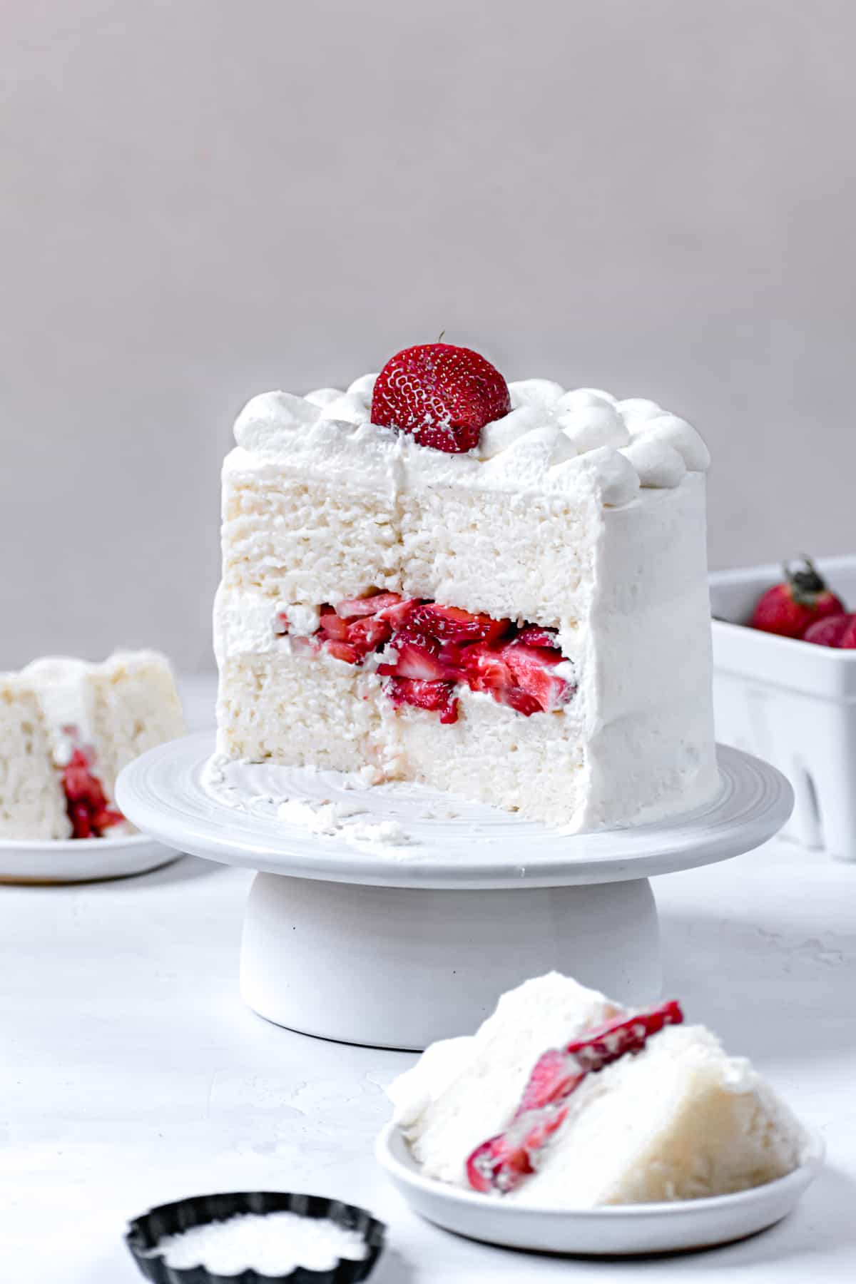 sliced cake on white cake stand to reveal texture of cake and fresh strawberry filling.