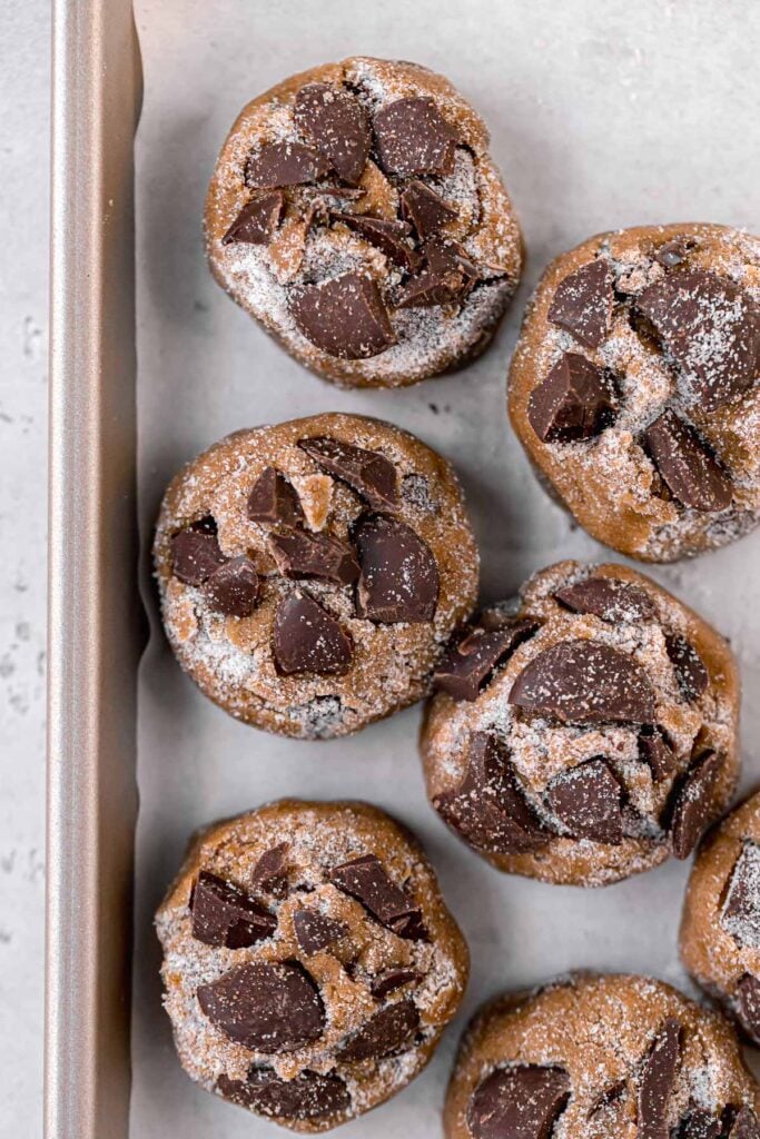 cookie dough rolled in sugar and extra chocolate pressed on top lined up on baking sheet