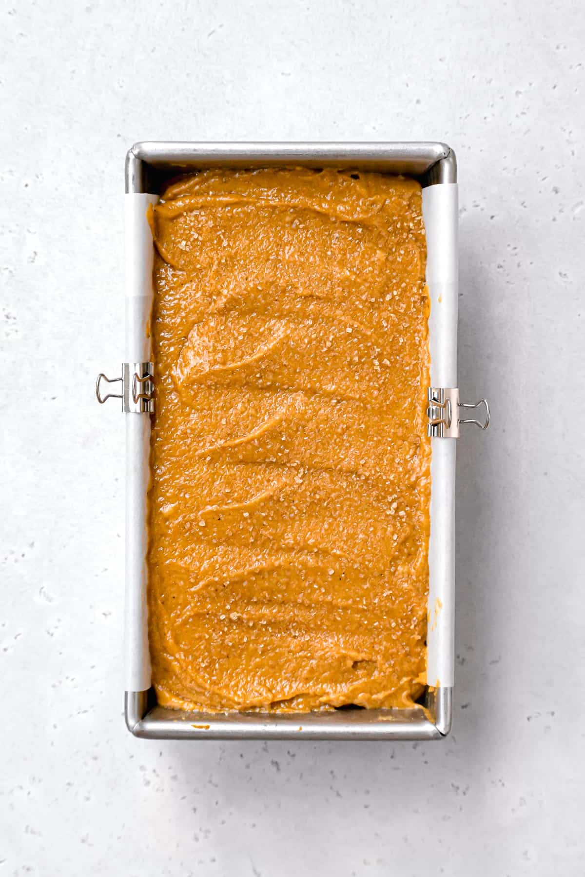 pumpkin bread batter with turbinado sugar on top in metal loaf pan.