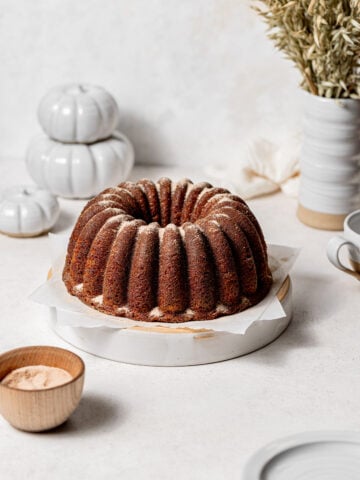 apple cider bundt cake coated in cinnamon sugar on white plate.