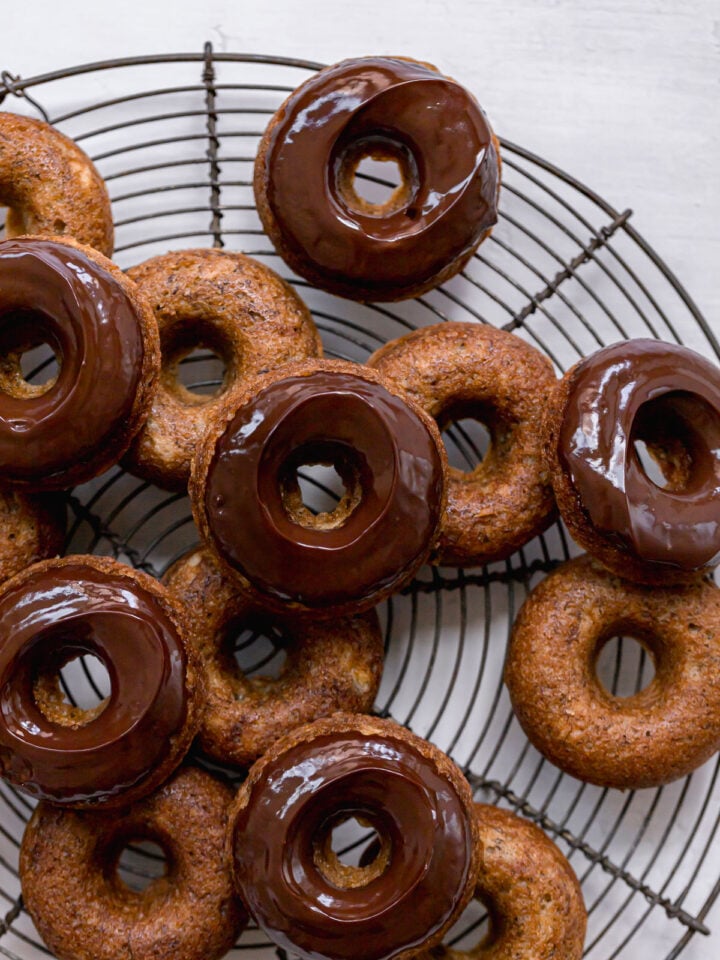 chocolate glazed banana bread donuts piled on round wire rack