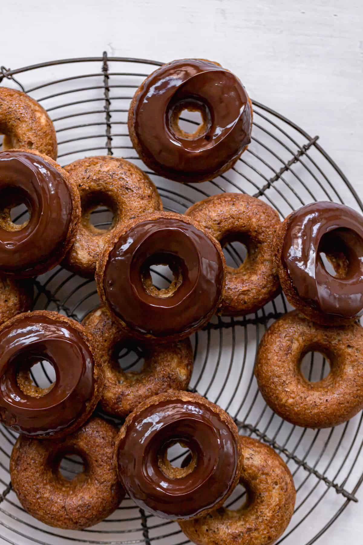 chocolate glazed banana bread donuts piled on round wire rack.