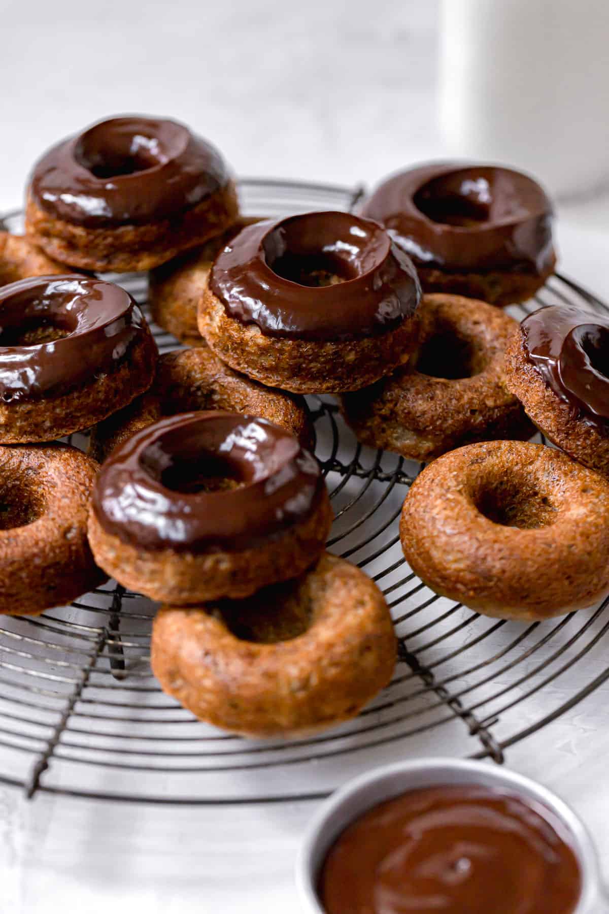 chocolate glazed donuts piled on round wire rack.