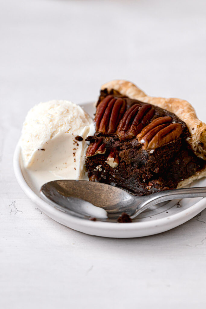slice of chocolate brownie pie on white plate with scoop of vanilla ice cream
