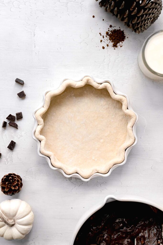 unbaked pie crust in white pie dish with bowl of brownie batter