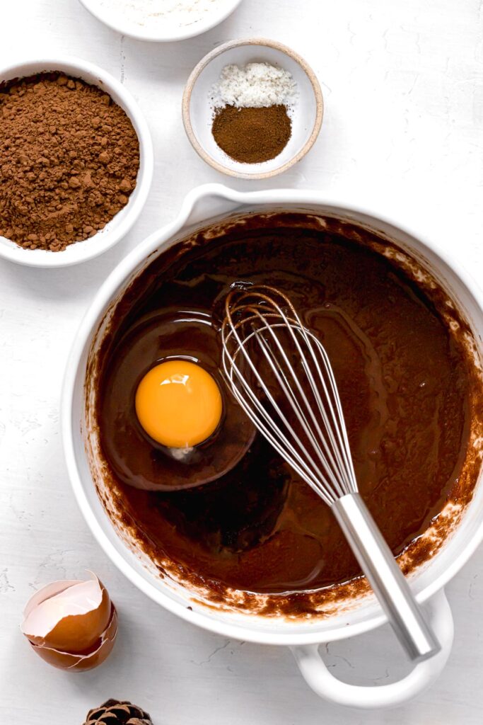 egg and vanilla added to brownie batter in white bowl