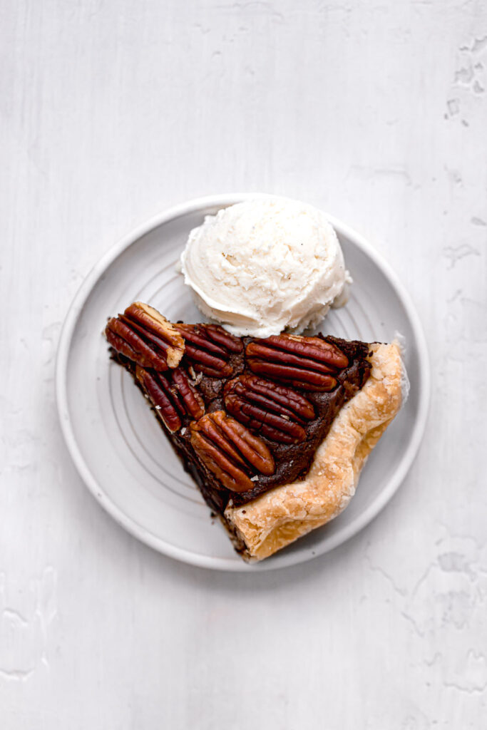 slice of pecan brownie pie on white plate with scoop of vanilla ice cream